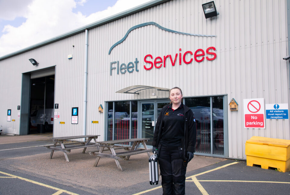 Female apprentice employee standing outside of the fleet services building, holding a toolkit.